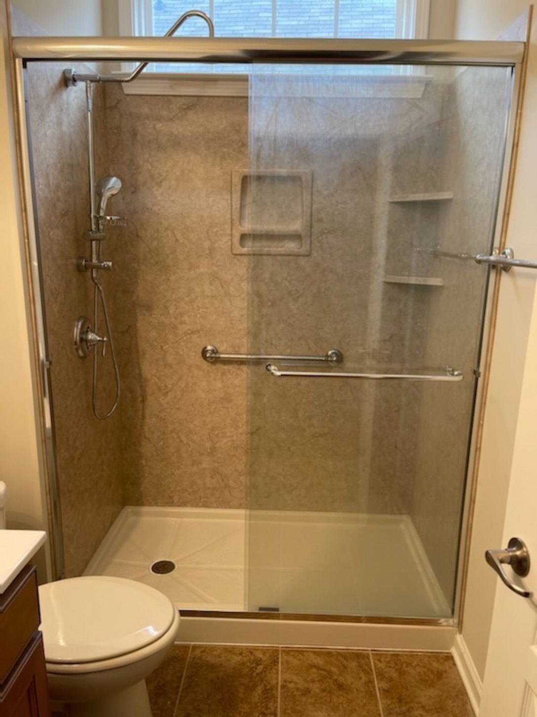 Warm stone-look shower with a clear glass enclosure and built-in storage niches
